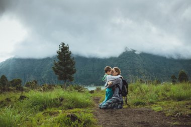 Genç kadın oğlunu dağ ve göl bir arka plan üzerinde sarılma