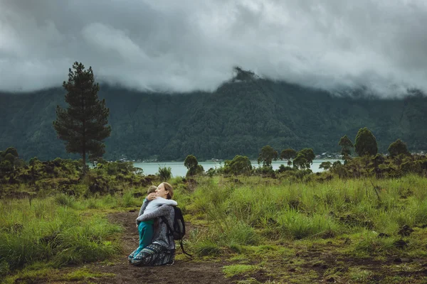 Genç kadın oğlunu dağ ve göl bir arka plan üzerinde sarılma