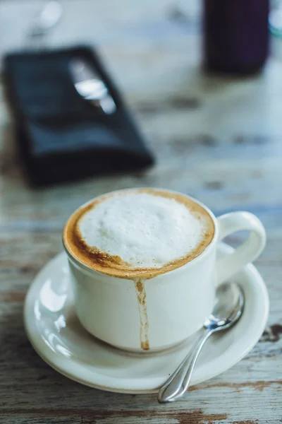 Zamknij się z filiżanki cappuccino leżącego na drewnianym stole w pobliżu mobil — Zdjęcie stockowe