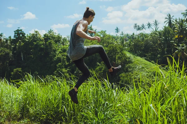 Jovem pulando de um penhasco com os braços erguidos — Fotografia de Stock