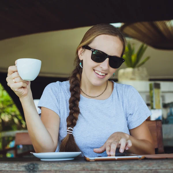 Young woman drinking coffee and watching at tablet at restaurant — 스톡 사진