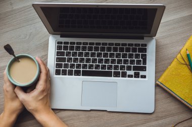 Ahşap backgr üzerinde oturan kızın elinde laptop ve kahve Kupası