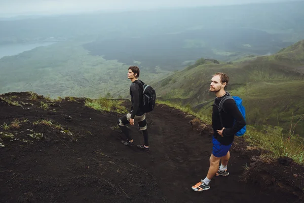 3 Männer laufen mit Rucksäcken und weißen Wolken den Hügel entlang. — Stockfoto