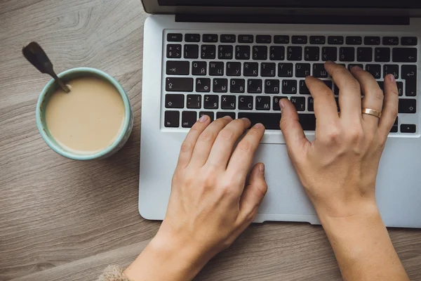 Laptop e xícara de café nas mãos da menina sentado em um backgr de madeira — Fotografia de Stock