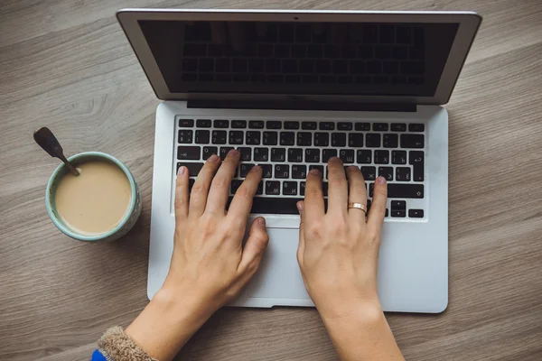 Laptop e xícara de café nas mãos da menina sentado em um backgr de madeira — Fotografia de Stock