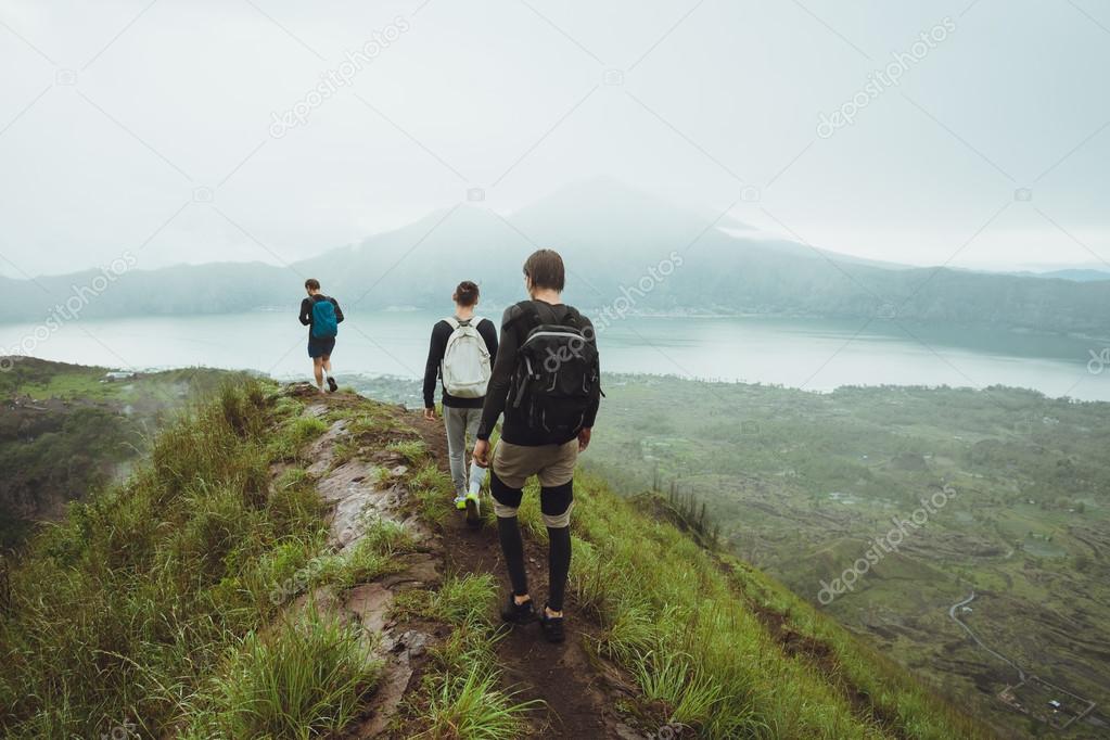 3 Men walk along the hill with backpacks and with white clouds a