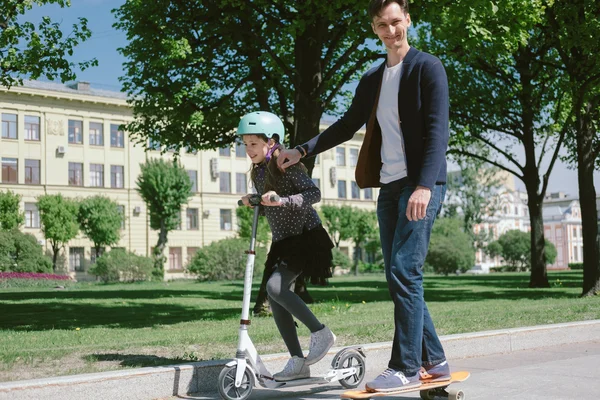 Apa és lánya ride a scooter és a skate együtt — Stock Fotó