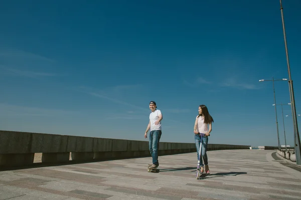 Jonge vrouw rijden een Scooter met haar echtgenoot op een Skateboard. A — Stockfoto