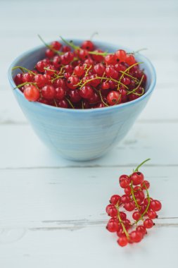 Beyaz ahşap bir masa üzerinde mavi bir kova kırmızı kuş üzümü
