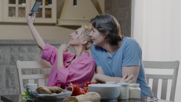 부부가 셀카 사진을 전화로 찍고 함께 저녁을 먹는다. 즐거운 남녀 와인 잔을 들고 집에서 음식을 먹는 모습 — 비디오