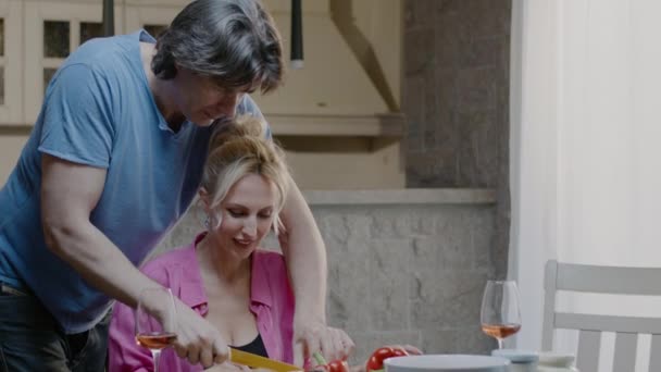 Gut aussehendes Paar bereitet zu Hause Essen zu. Schöner Mann und blonde Frau mit einem Glas Wein essen in der Küche — Stockvideo