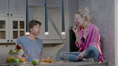 Meyve yiyen mutlu çift birlikte eğleniyor ve sağlıklı kahvaltı yapıyor. Erkek ve kadın mutfakta konuşur ve güler.