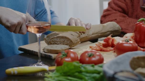Zbliżenie męska ręka przygotowuje sałatkę spożywczą i krojony chleb. Rodzinna para z winem jedzą kolację w domu. — Wideo stockowe