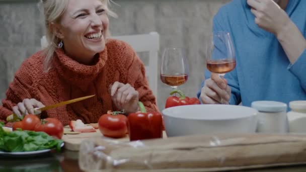 Щаслива сімейна пара готує їжу вдома. Красивий чоловік і блондинка з келихом вина обідають на кухні — стокове відео