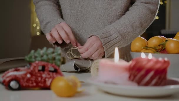 Γυναικεία χέρια κάνουν βιολογική συσκευασία Χριστούγεννα ή το νέο έτος δώρο στο τραπέζι με κερί και μανταρίνια — Αρχείο Βίντεο