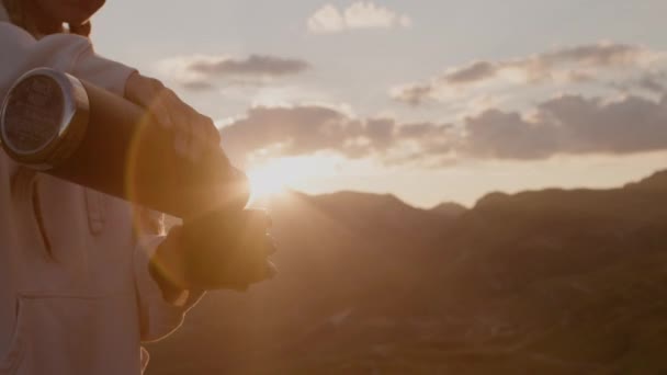 Mujer viajera con rastas bebe té caliente del termo y mira el amanecer desde la montaña. — Vídeos de Stock