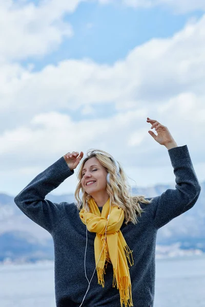 Mulher loira feliz usando fones de ouvido ouvindo podcast de música positiva do aplicativo de smartphone contra o mar Imagens De Bancos De Imagens