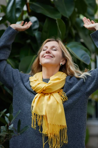 Happy blonde woman with yellow scarf and her hair blowing in the breeze stands near sea Stock Picture