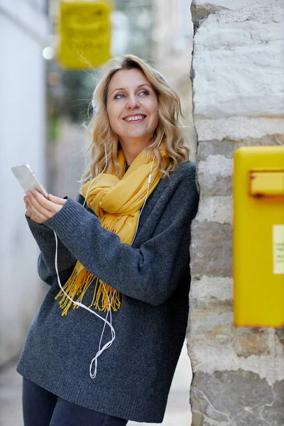 Glad blond kvinna bär hörlurar lyssna positiv musik podcast från smartphone ansökan Royaltyfria Stockbilder