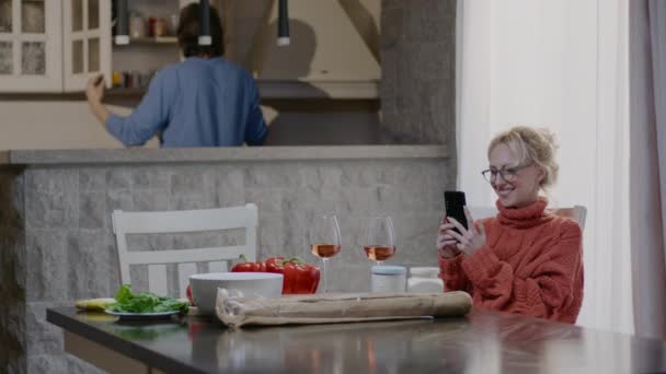 Glückliches Familienpaar beim Zubereiten des Essens zu Hause. Schöner Mann und blonde Frau mit einem Glas Wein essen in der Küche — Stockvideo