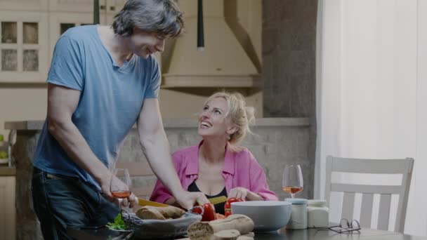 Feliz pareja activa de la familia preparando la comida y reír en casa. Hombre guapo y mujer rubia cenan con vino — Vídeos de Stock