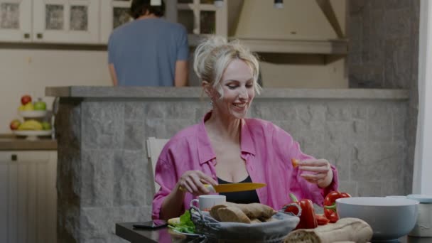 Gelukkige familie koppel bereidt eten thuis. Knappe man en blonde vrouw met glas wijn dineren in de keuken — Stockvideo
