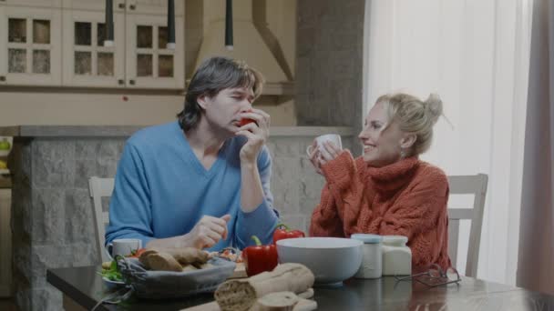 Mutlu aktif aile çifti evde yemek hazırlıyor ve gülüyor. Yakışıklı adam ve sarışın kadın akşam yemeğini şarapla yiyorlar. — Stok video