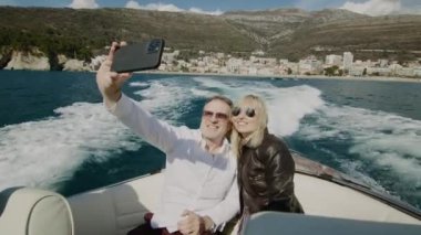 Güneş gözlüklü mutlu romantik çift açık denizde yelken açan motorlu teknede selfie videosu çekiyor. Kadın ve erkek tatilde gemi seyahatinde cep telefonu fotoğrafları çekiyorlar..