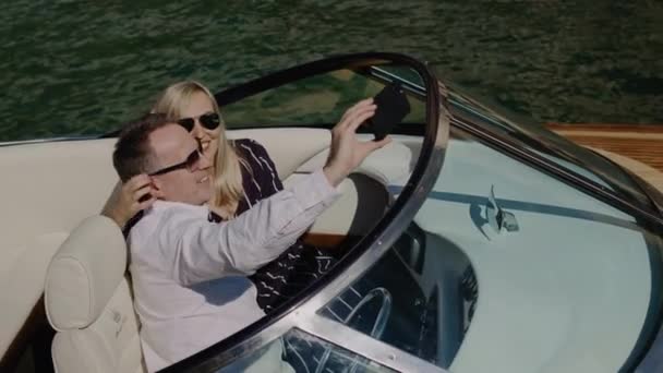 Glada romantiska par i solglasögon ta selfie video på motorbåt fartyg seglar på öppet hav. Kvinna och man ta mobiltelefon bilder på fartyg resa under semestern. — Stockvideo
