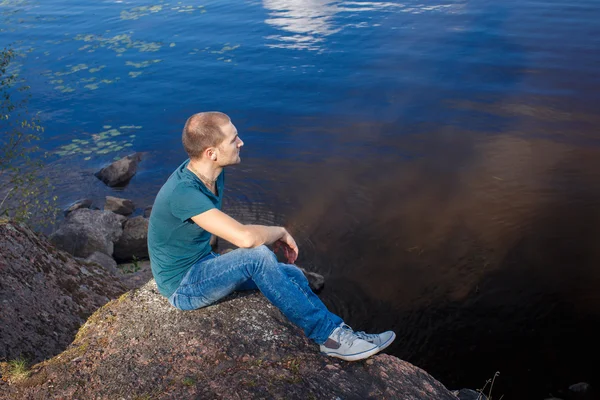Θλιβερή άνδρα καθισμένο σε βράχο, δίπλα στη λίμνη — Φωτογραφία Αρχείου