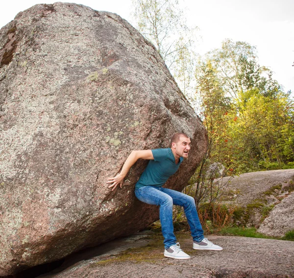 Homem com mochila empurrando uma pedra enorme — Fotografia de Stock