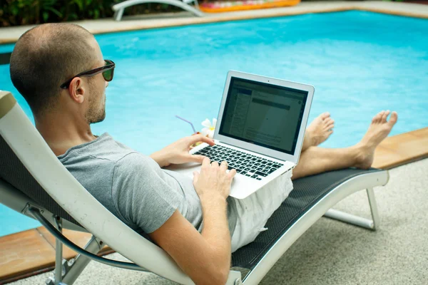 Um homem a trabalhar no computador ao lado da piscina — Fotografia de Stock