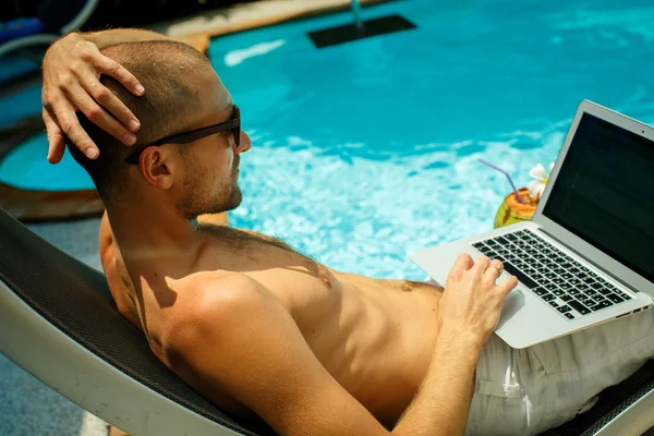 Человек, работающий за компьютером у бассейна — стоковое фото