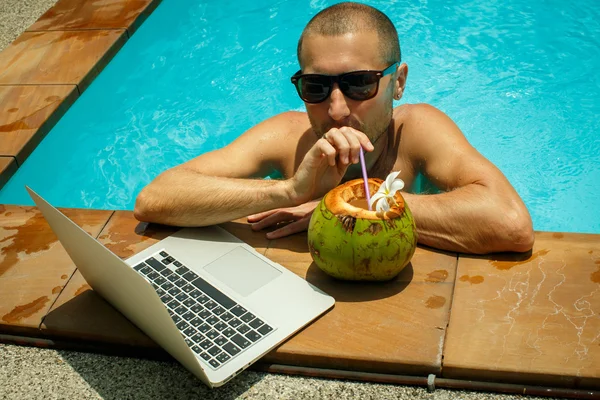 Un homme travaillant à l'ordinateur à côté de la piscine — Photo