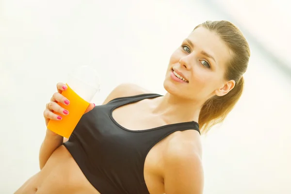 Bella donna in abbigliamento sportivo bere succo di frutta sulla spiaggia . — Foto Stock