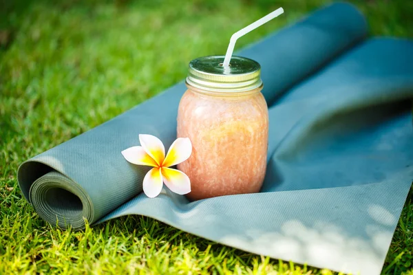 果汁和瑜伽垫在草地上 免版税图库图片