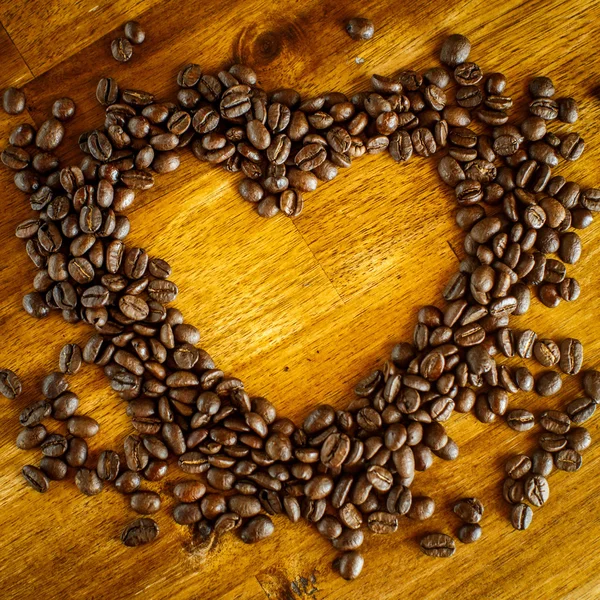 Форма сердца из кофейных зерен на деревянной поверхности. — стоковое фото