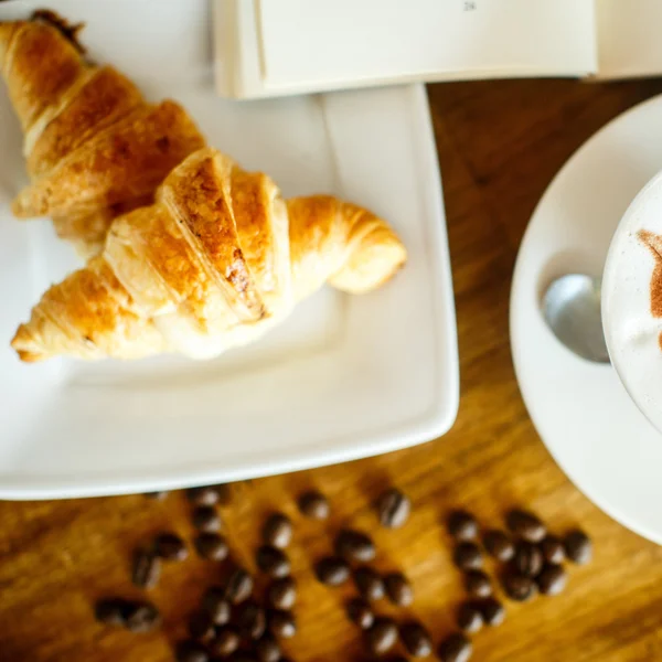 Cappuccino und Croissant mit Kaffeebohnen und Büchern — Stockfoto
