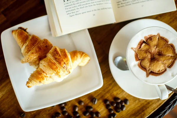 Cappuccino and croissant with coffee bean and books — Zdjęcie stockowe