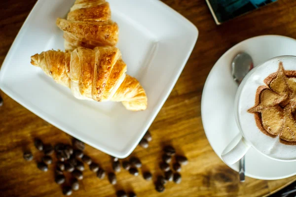 Cappuccino e croissant com grão de café — Fotografia de Stock