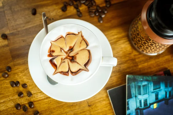 Cappuccino mit frischen Kaffeebohnen, Wasser und Büchern auf einem braunen B — Stockfoto