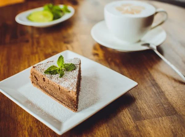 Bolo de chocolate com um cappuccino em uma mesa de madeira em uma restaura — Fotografia de Stock