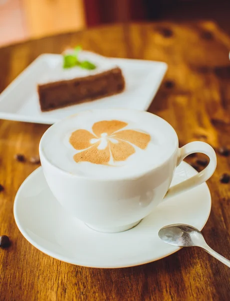 Bolo de chocolate com um cappuccino em uma mesa de madeira em uma restaura — Fotografia de Stock