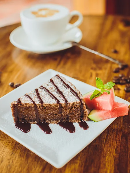 Bolo de chocolate com um cappuccino em uma mesa de madeira em uma restaura — Fotografia de Stock