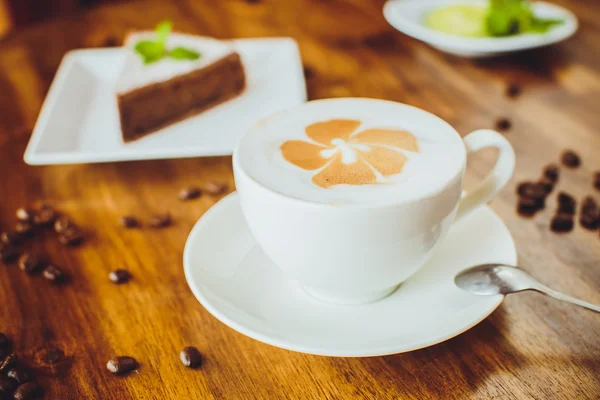 Bolo de chocolate com um cappuccino em uma mesa de madeira em uma restaura — Fotografia de Stock