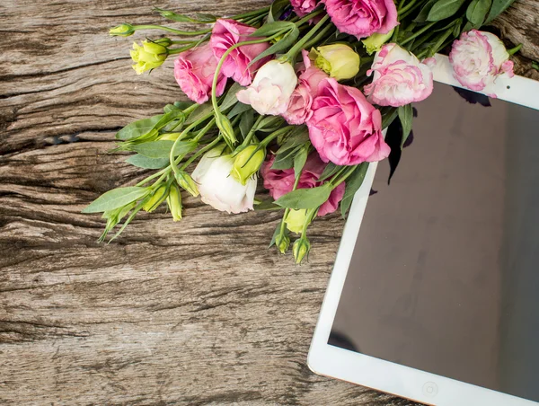 Buquê de flores em uma mesa de madeira com um tablet sagacidade — Fotografia de Stock