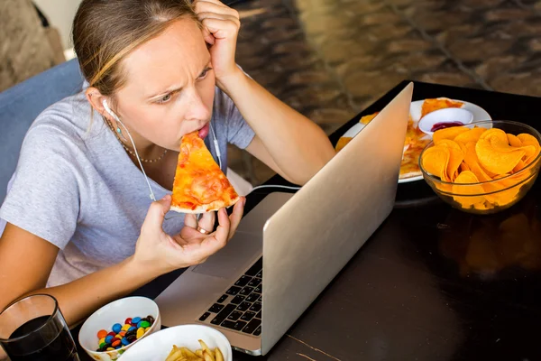 Una donna lavora al computer e mangia fast food. Vita malsana — Foto Stock