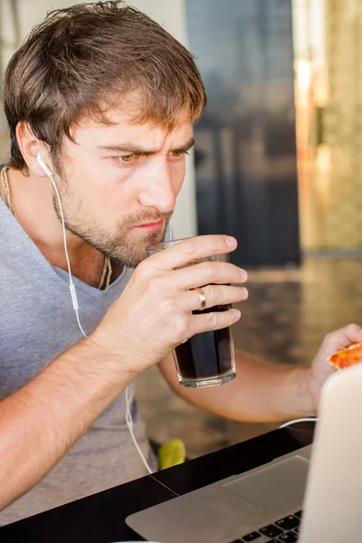 Чоловік працює за комп'ютером і їсть фастфуд. Нездорове життя — стокове фото