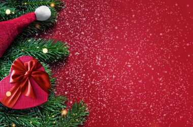 Kırmızı arka plan, köknar dalları, Noel Baba şapkası ve hediye kutusu. Noel süsü. Tatil kavramı.