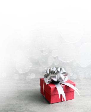 Gri arka planda gümüş kurdeleli tek bir kırmızı hediye kutusu.